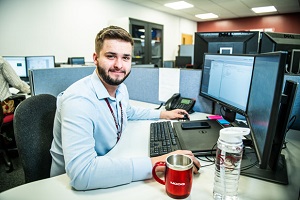Associate Engineer Tom sits at his desk, working on a project. He has a Moog mug and water bottle next to him.